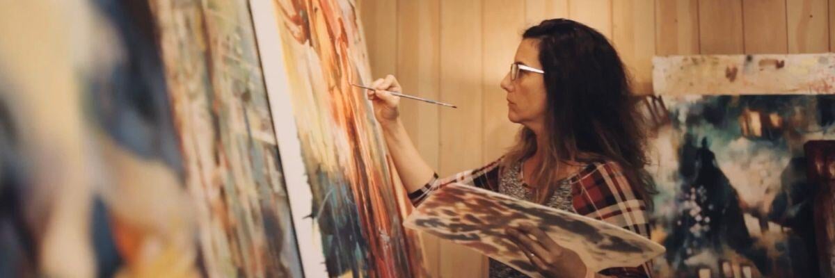 Elli Milan painting woman painting infront of yellow brown tan canvases
